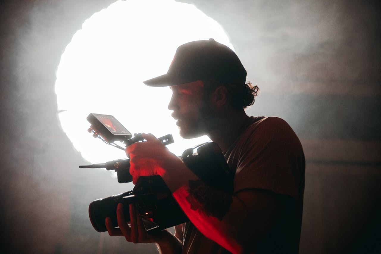 Silhouette of a cinematographer filming with a camera in a smoky setting, dramatic lighting.